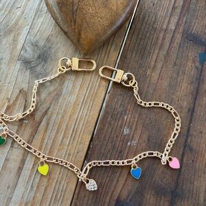 Gold tone phone  accessory with enameled colored hearts .